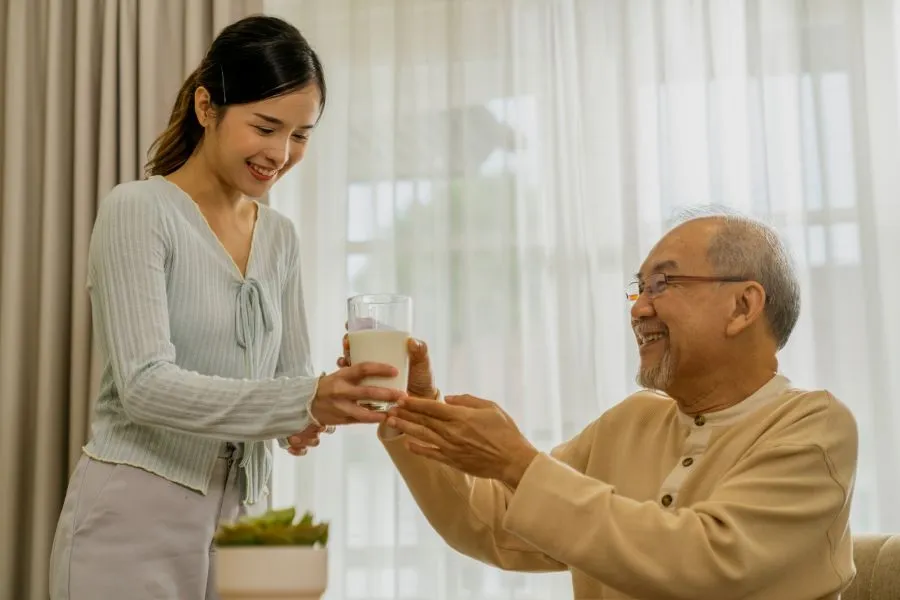 A young woman passes a glass of milk to an elderly man.